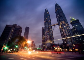 The Petronas Twin Towers in Kuala Lumpur lit up at dusk, with light trails from passing traffic in the foreground.