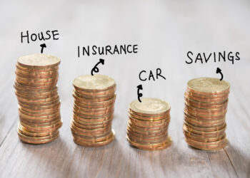 Four stacks of coins labeled "House," "Insurance," "Car," and "Savings" on a wooden surface, illustrating different financial categories or budgeting goals. | MyWebInsurance