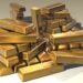 A large pile of shiny gold bars stacked haphazardly on a neutral surface, reflecting light and showing some surface scratches. | MyWebInsurance